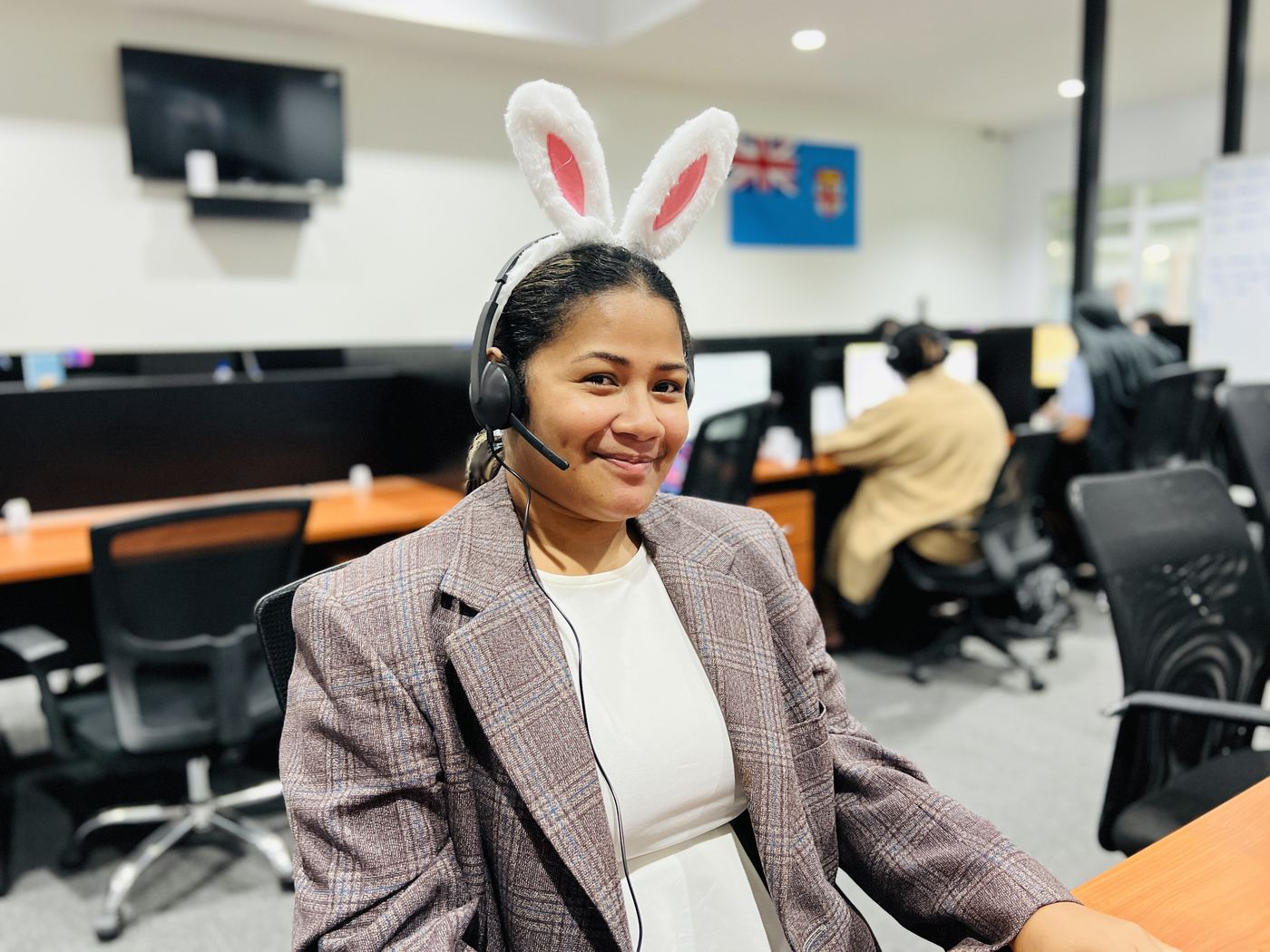 A NexOutsource customer experience agent at her workstation on the Suva floor, headset on